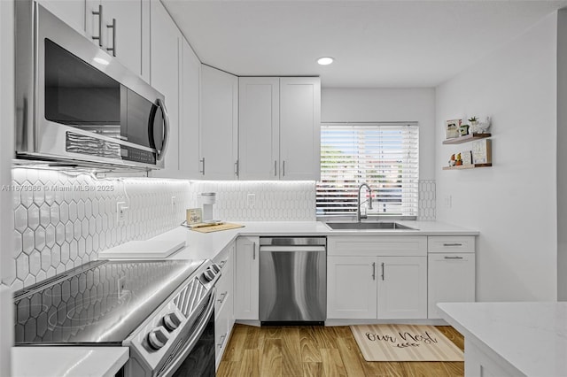 kitchen featuring sink, appliances with stainless steel finishes, backsplash, white cabinets, and light wood-type flooring