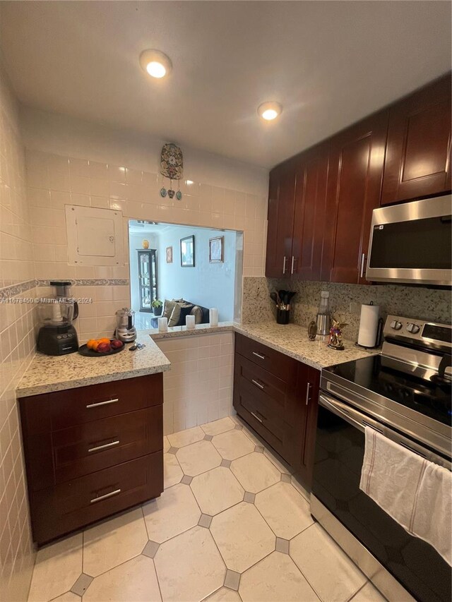 kitchen with backsplash, appliances with stainless steel finishes, light tile patterned floors, and light stone counters