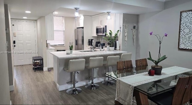 kitchen with appliances with stainless steel finishes, light hardwood / wood-style floors, white cabinetry, and a breakfast bar area