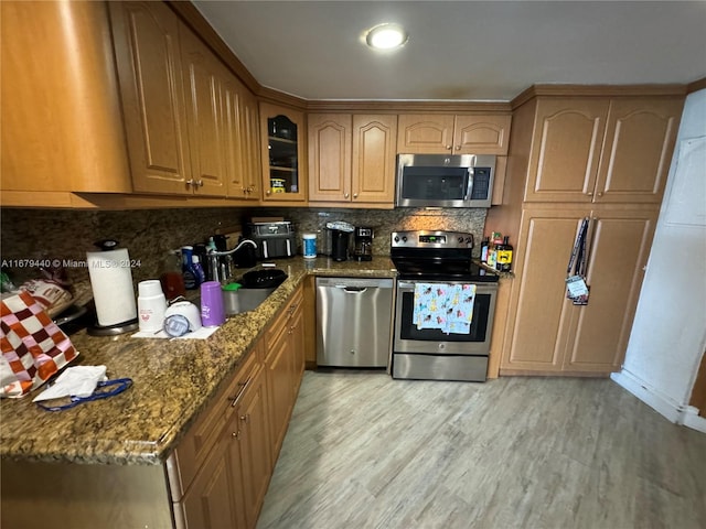 kitchen featuring tasteful backsplash, light hardwood / wood-style flooring, dark stone countertops, sink, and stainless steel appliances