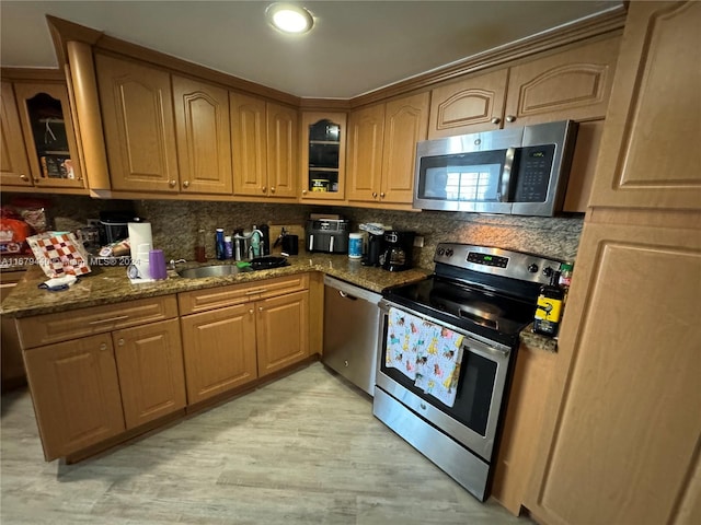 kitchen featuring appliances with stainless steel finishes, sink, backsplash, dark stone countertops, and light hardwood / wood-style flooring