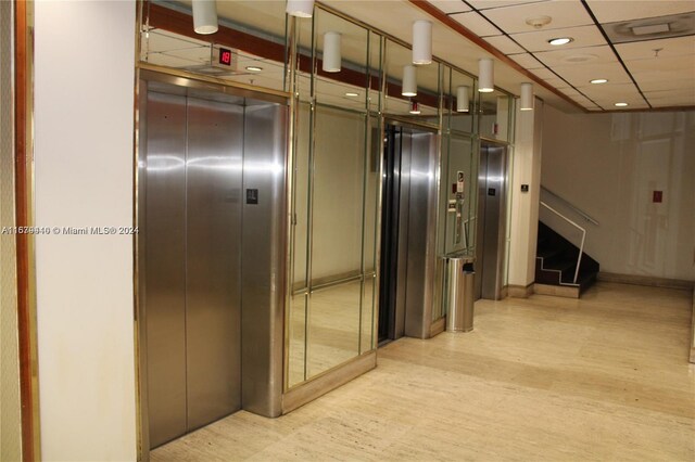 hallway featuring light hardwood / wood-style flooring, a paneled ceiling, and elevator