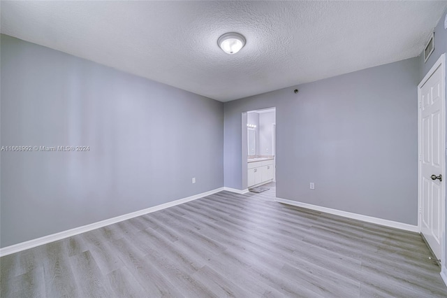 unfurnished bedroom with connected bathroom, a textured ceiling, and light wood-type flooring