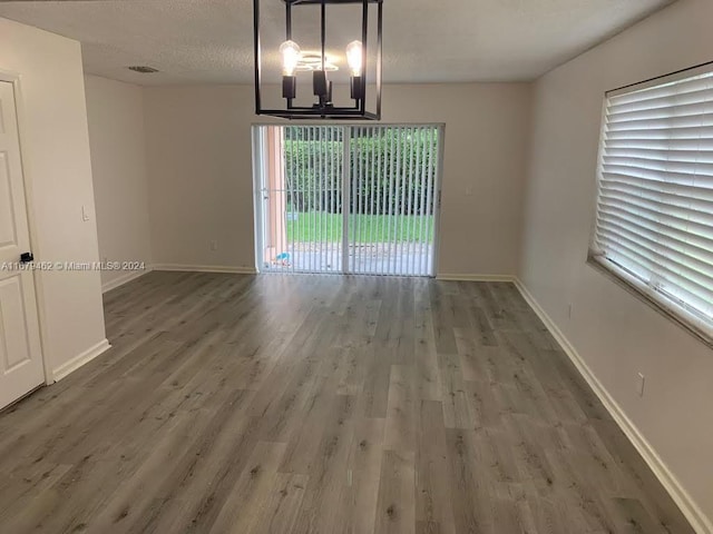 unfurnished dining area featuring a textured ceiling, an inviting chandelier, and dark hardwood / wood-style floors