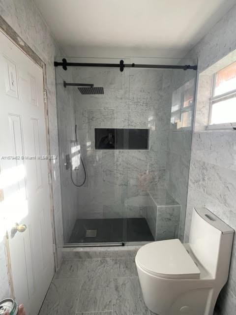 bathroom with toilet, tile walls, and a shower with shower door