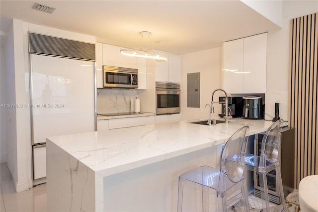 kitchen with appliances with stainless steel finishes, kitchen peninsula, white cabinets, and sink