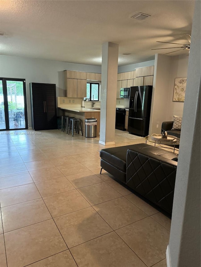 kitchen featuring light brown cabinetry, sink, black appliances, ceiling fan, and light tile patterned floors