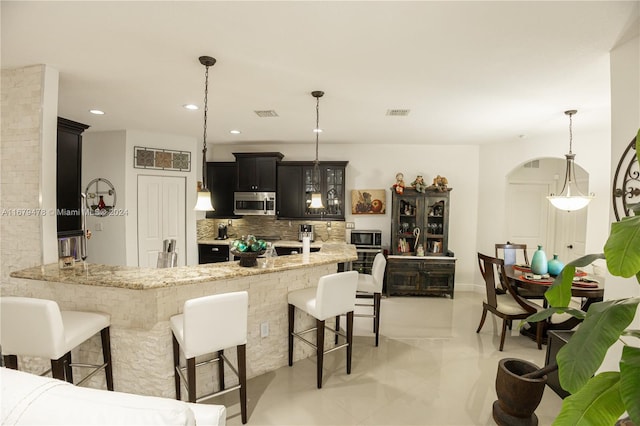 kitchen with kitchen peninsula, backsplash, light stone countertops, a kitchen bar, and pendant lighting