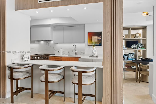 kitchen featuring a breakfast bar, sink, stainless steel stove, gray cabinets, and kitchen peninsula