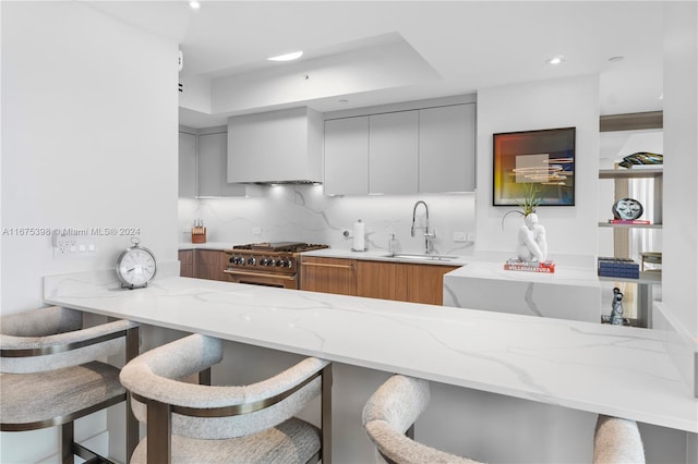 kitchen with gray cabinetry, a kitchen breakfast bar, sink, light stone countertops, and high end stove