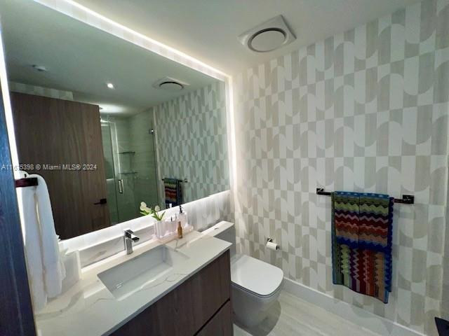 bathroom featuring vanity, toilet, a shower with door, and tile walls