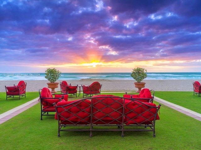 patio terrace at dusk featuring a beach view, a water view, and a yard