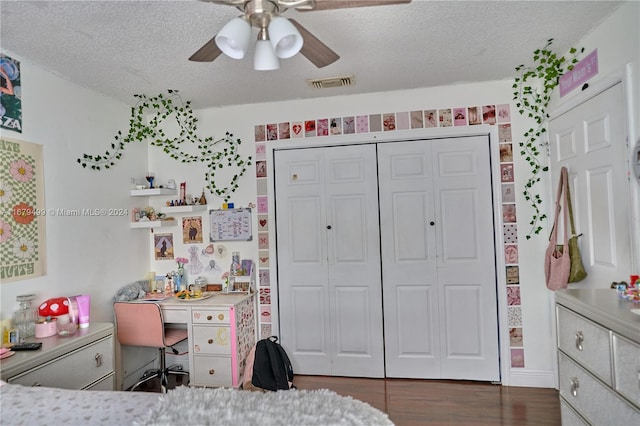 bedroom featuring built in desk, ceiling fan, a textured ceiling, dark wood-type flooring, and a closet