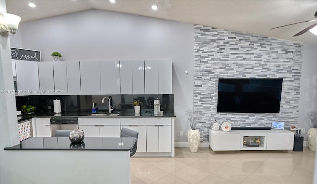 kitchen with sink, kitchen peninsula, lofted ceiling, stainless steel dishwasher, and white cabinets