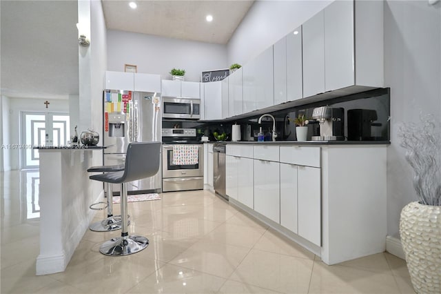 kitchen featuring stainless steel appliances, white cabinets, dark countertops, a sink, and a breakfast bar area