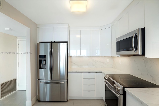 kitchen with stainless steel appliances, light tile patterned flooring, white cabinetry, and light stone counters