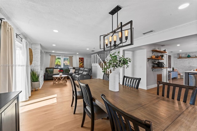 dining area featuring ornamental molding, light hardwood / wood-style flooring, a textured ceiling, and an inviting chandelier