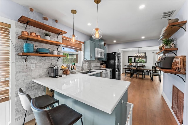 kitchen featuring kitchen peninsula, stainless steel electric stove, a kitchen bar, decorative light fixtures, and light hardwood / wood-style floors