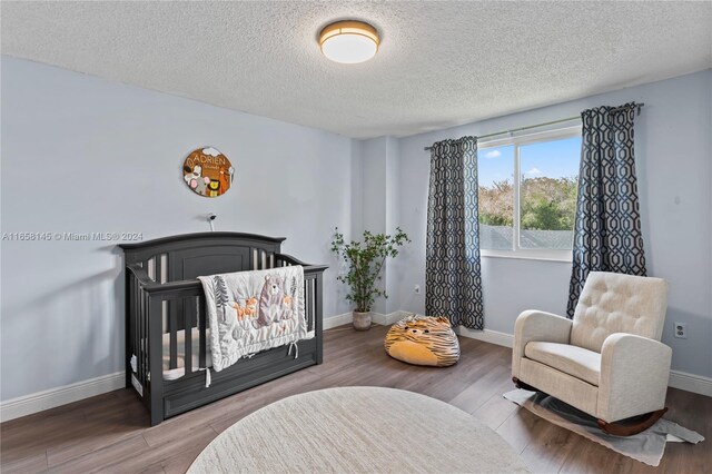 bedroom featuring a textured ceiling, a nursery area, and wood-type flooring