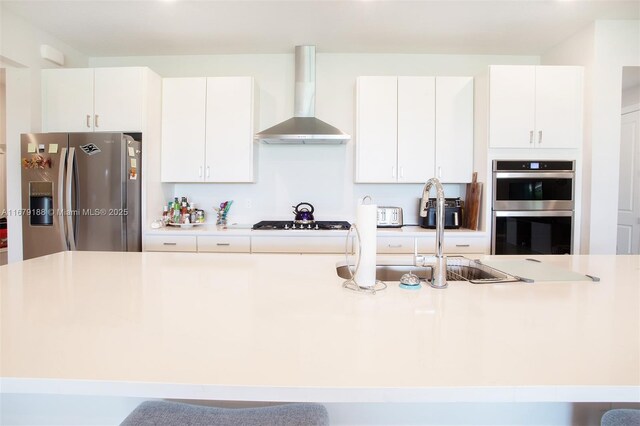 kitchen with stainless steel appliances, wall chimney range hood, a breakfast bar, and white cabinets