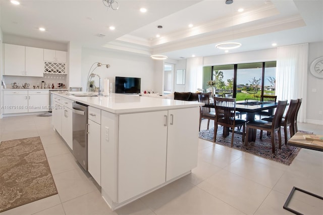 kitchen with light countertops, a tray ceiling, a center island with sink, and white cabinetry