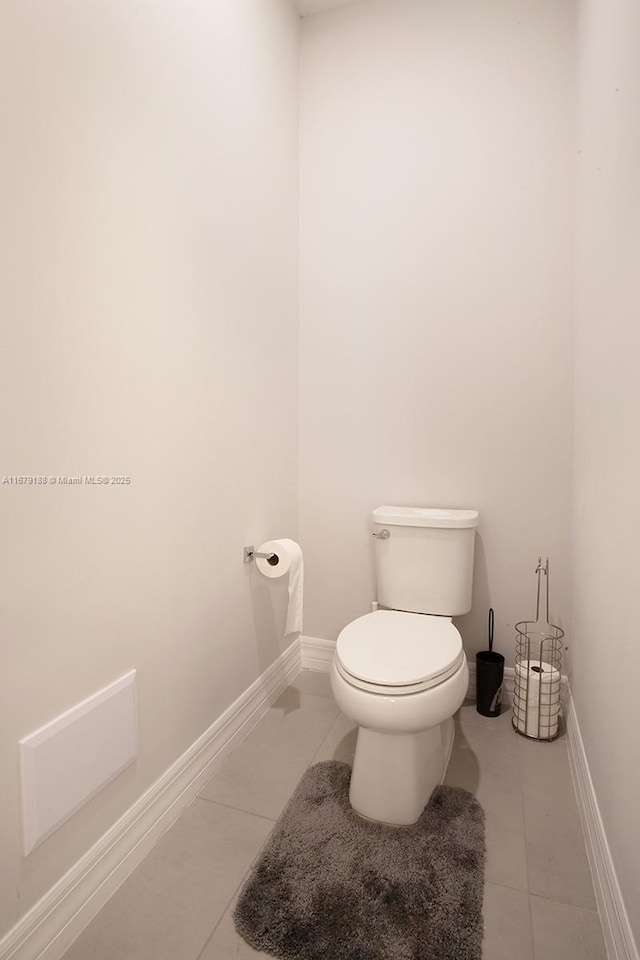 half bathroom with toilet, baseboards, and tile patterned floors