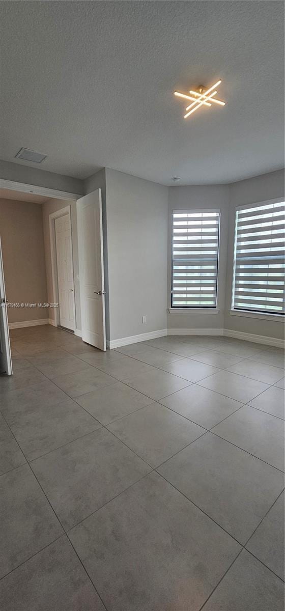 empty room with a textured ceiling, tile patterned floors, visible vents, and baseboards