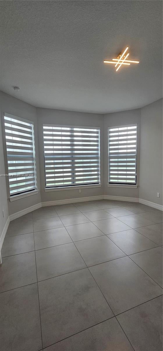 tiled spare room featuring a textured ceiling and baseboards