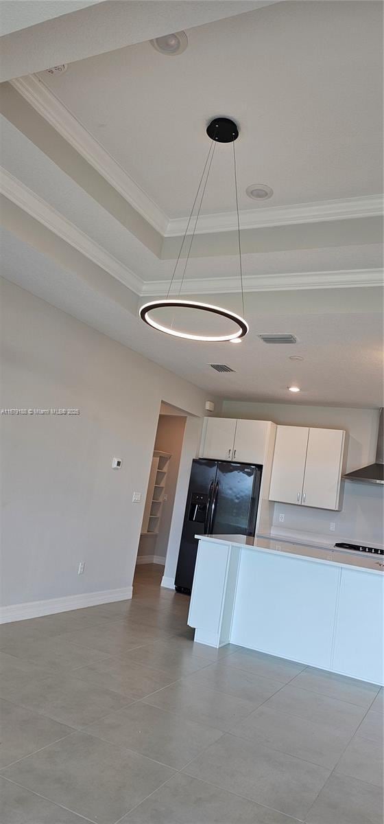 kitchen with a raised ceiling, light countertops, hanging light fixtures, ornamental molding, and white cabinets