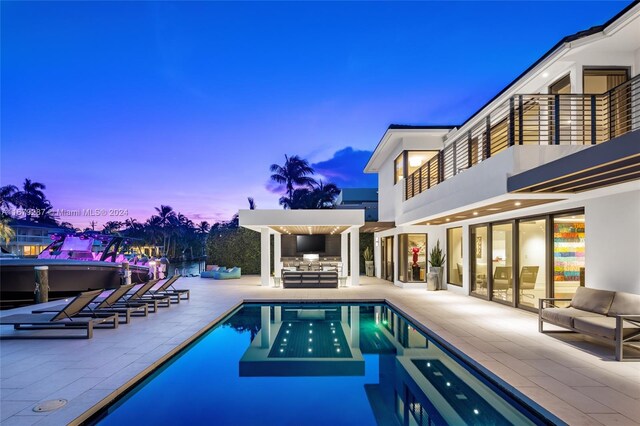 pool at dusk with a patio area and an outdoor living space