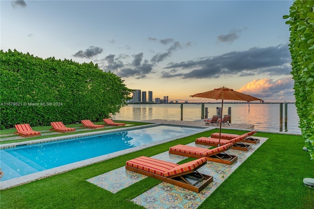 pool at dusk with a yard, a water view, and a patio