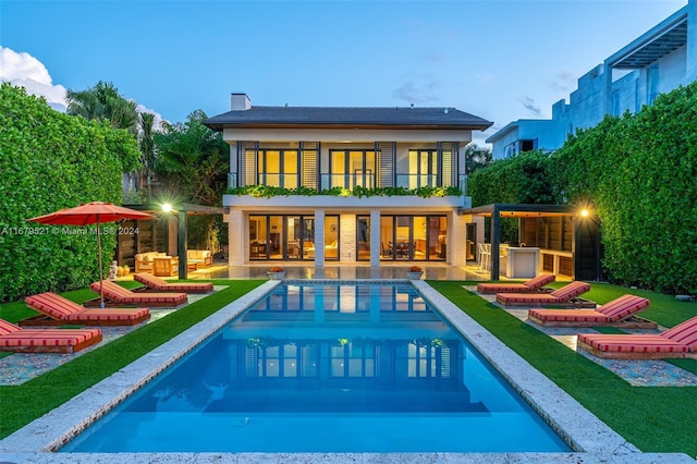 back house at dusk with a lawn, an outdoor kitchen, a patio area, and a balcony