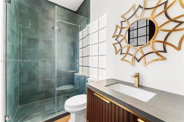 bathroom with a tile shower, hardwood / wood-style floors, vanity, and toilet