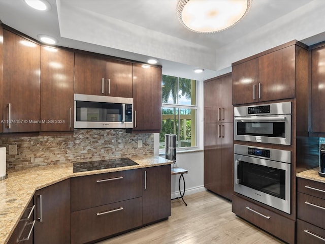 kitchen with appliances with stainless steel finishes, decorative backsplash, light stone countertops, and light wood-type flooring