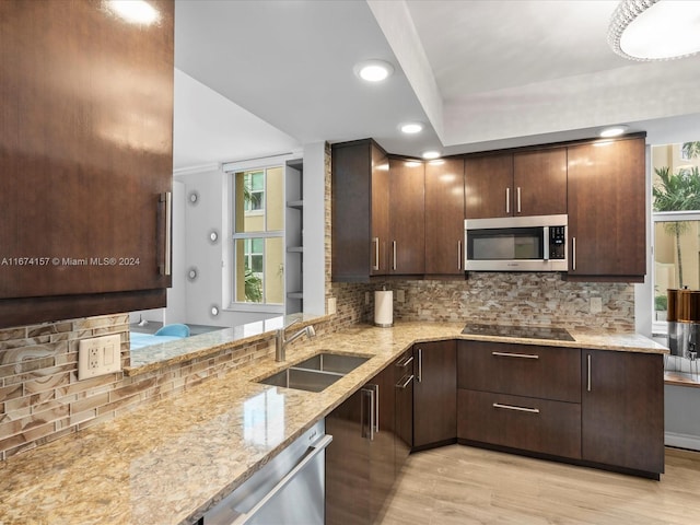 kitchen with backsplash, appliances with stainless steel finishes, light stone countertops, light hardwood / wood-style floors, and sink