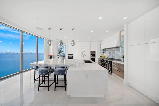 kitchen with a water view, white cabinets, high end range, pendant lighting, and a large island with sink