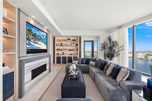 tiled living room with built in shelves, a premium fireplace, and a water view