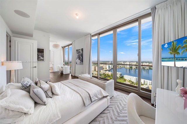 bedroom with floor to ceiling windows, a water view, and wood finished floors