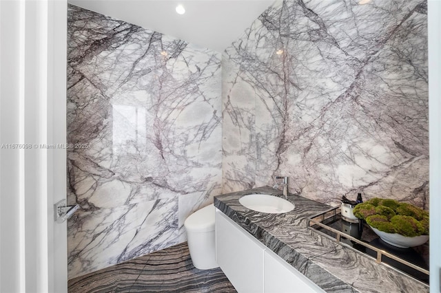 bathroom featuring recessed lighting, vanity, toilet, and stone wall