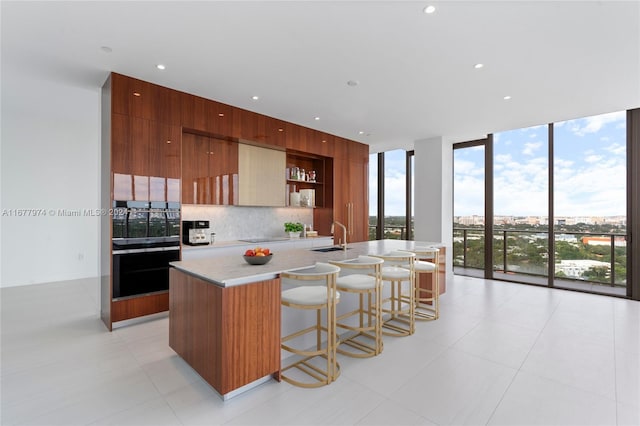 kitchen featuring a kitchen bar, tasteful backsplash, sink, light tile patterned floors, and an island with sink