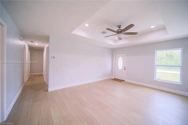 empty room featuring ceiling fan, light wood-type flooring, and a tray ceiling