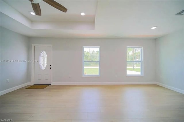 foyer entrance with a raised ceiling, ceiling fan, and light wood-type flooring