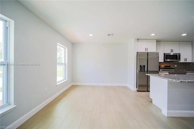 kitchen featuring appliances with stainless steel finishes, backsplash, stone countertops, white cabinets, and light hardwood / wood-style floors