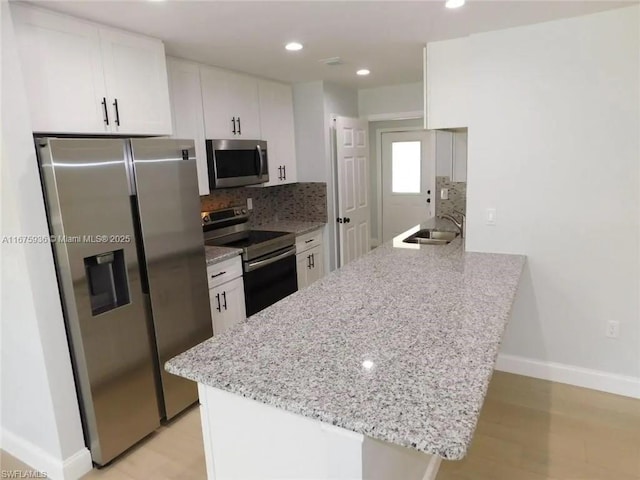 kitchen featuring white cabinetry, sink, light stone countertops, kitchen peninsula, and appliances with stainless steel finishes