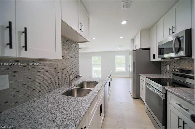 kitchen with backsplash, sink, light stone countertops, white cabinetry, and stainless steel appliances