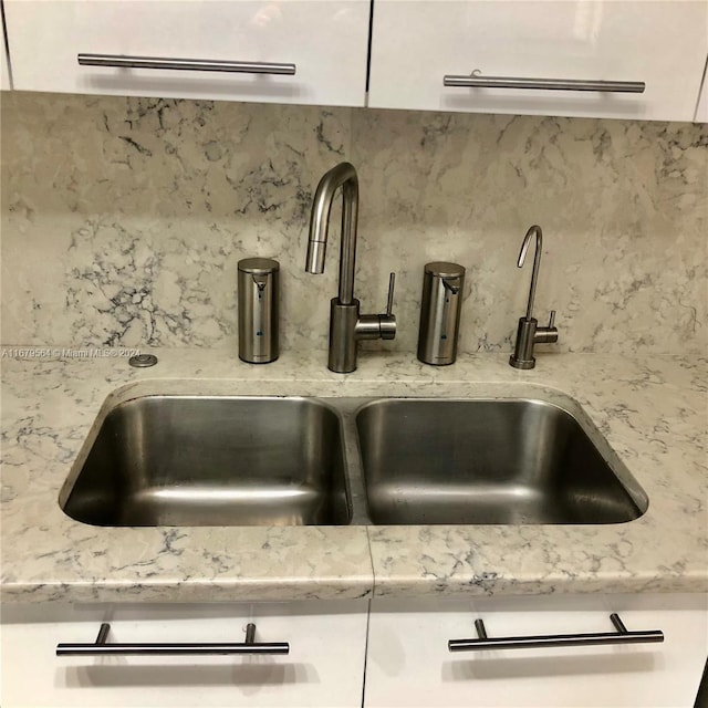 room details featuring light stone countertops, sink, and white cabinets