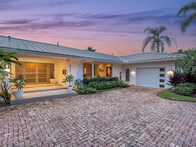 view of front facade featuring metal roof, a garage, decorative driveway, stucco siding, and a standing seam roof