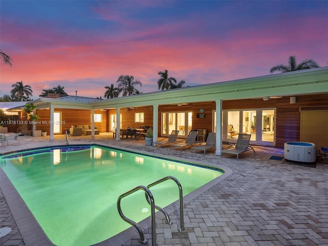 pool at dusk with french doors and a patio area