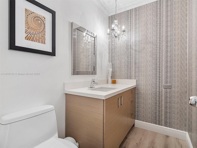 bathroom featuring toilet, ornamental molding, wood finished floors, a chandelier, and vanity