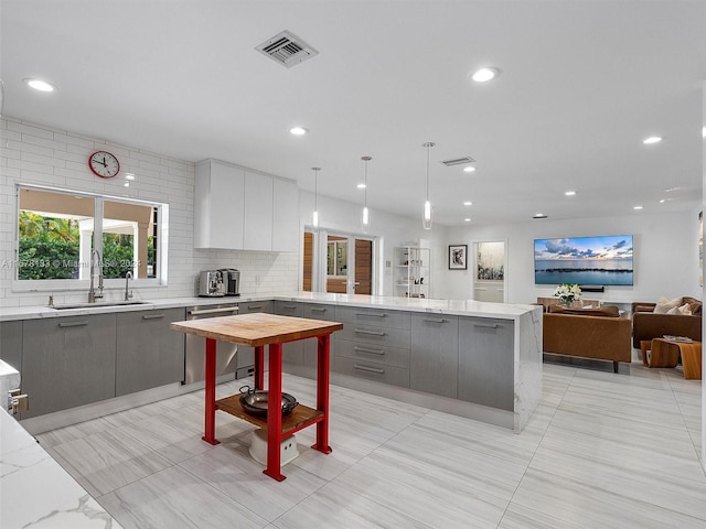 kitchen featuring stainless steel dishwasher, sink, light stone countertops, pendant lighting, and gray cabinets